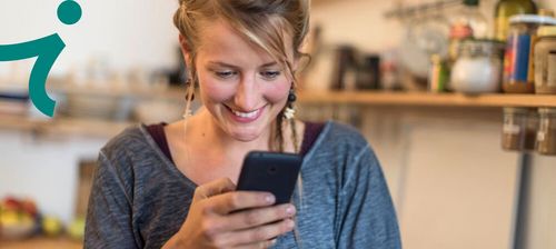 Junge Frau schaut lächelnd auf ihr Smartphone.