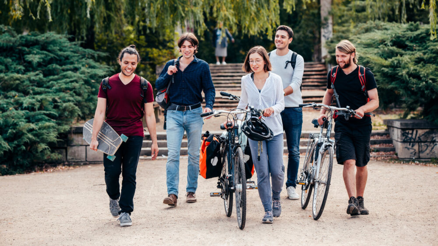 Eine Gruppe Studierender mit Fahrrädern und Skateboards laufen zusammen.