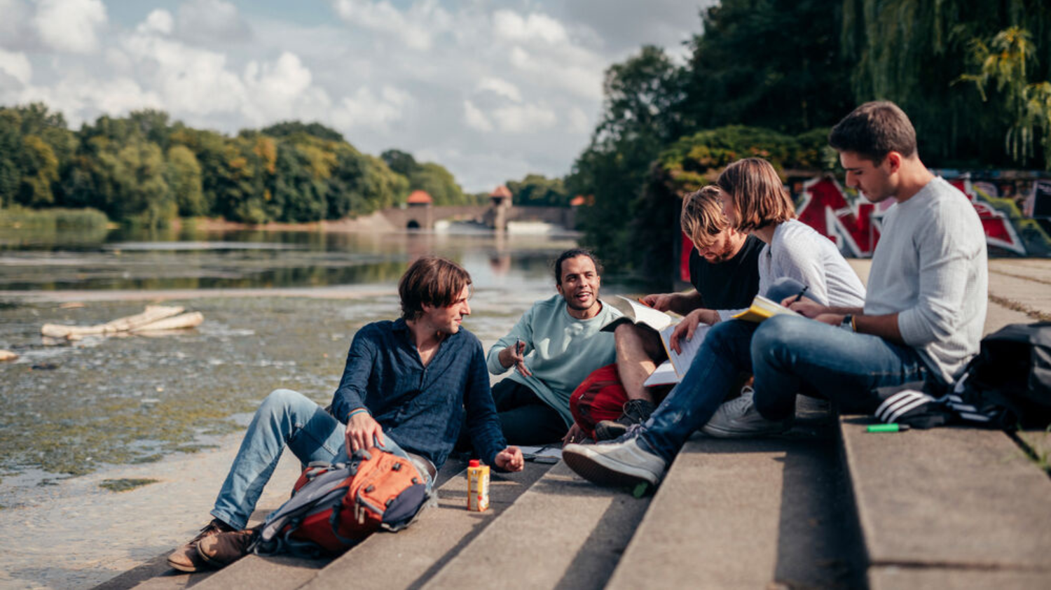 Eine Gruppe Studierender sitzen zusammen am Wasser und unterhalten sich.